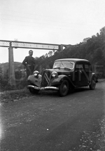 Un homme pose à côté de sa traction avant garée le long d'une route de montagne devant le viaduc des Fades.  - 1938